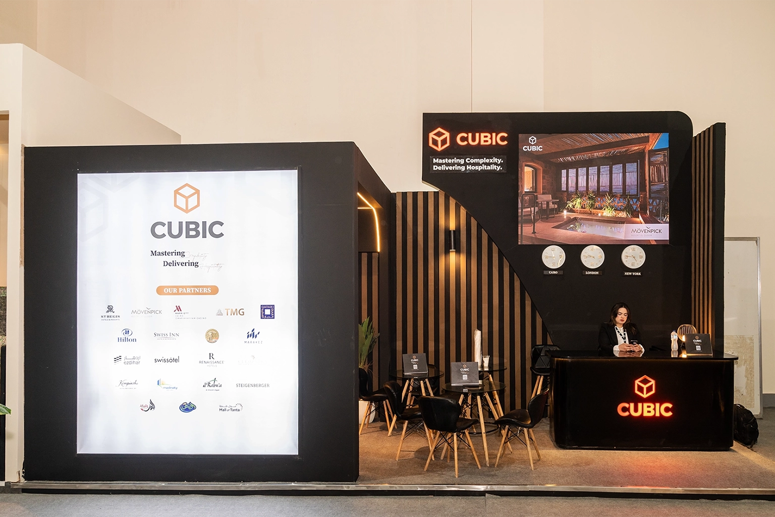 Custom-built exhibition stand with backlit branding, partner wall, hospitality seating, and reception counter at a trade show in Egypt