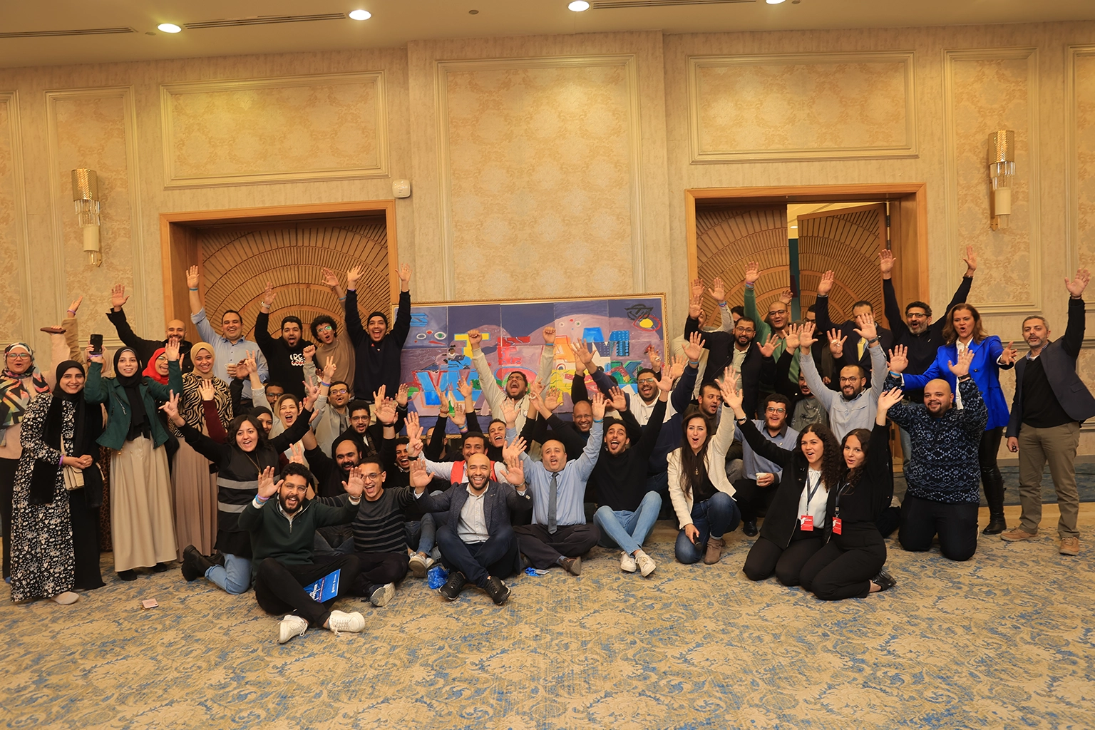 Full group photograph of employees at the close of a corporate team building day in Egypt, arranged in front of a branded backdrop